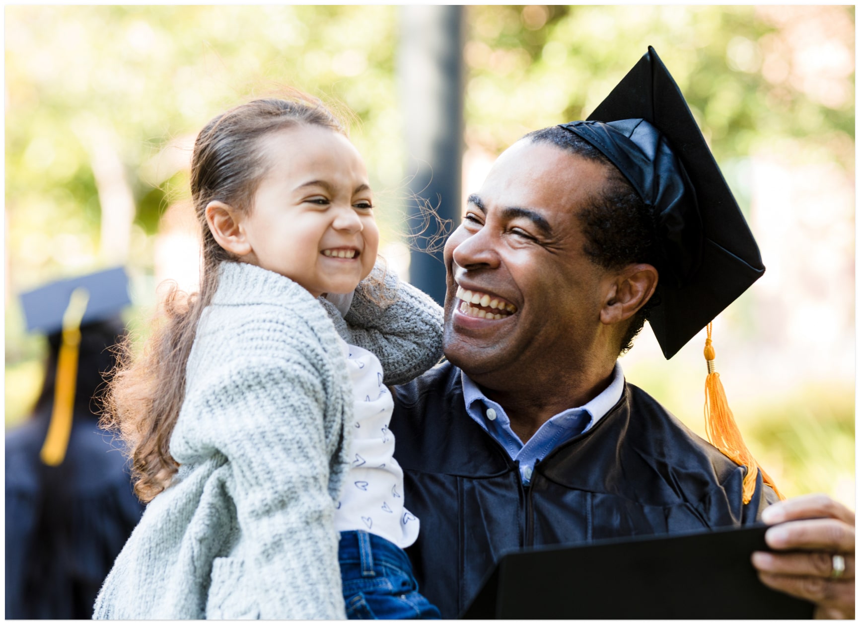 Happy caregiver in graduation robe holds smiling child
