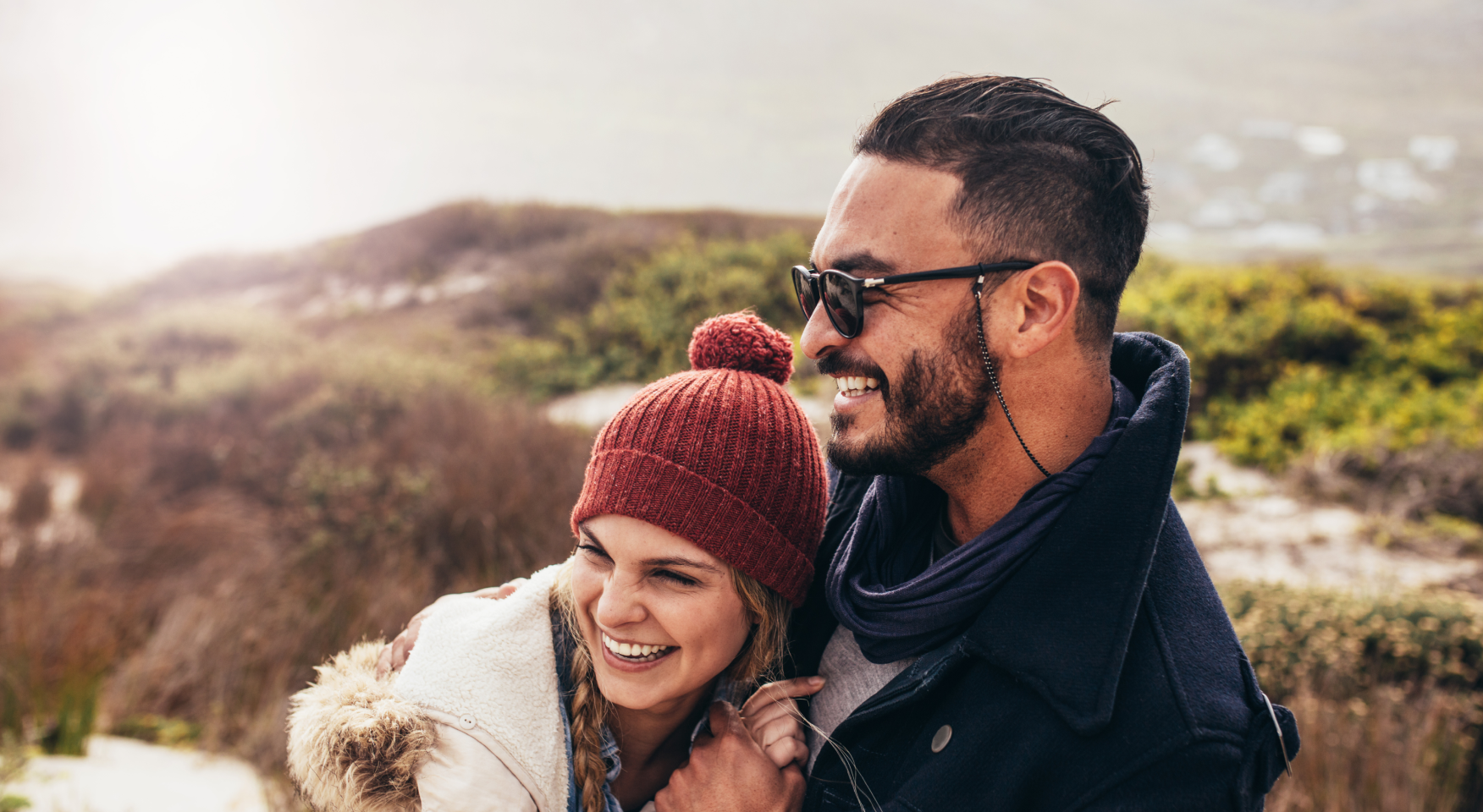 Two hikers smiling and hugging while gazing into the distance.