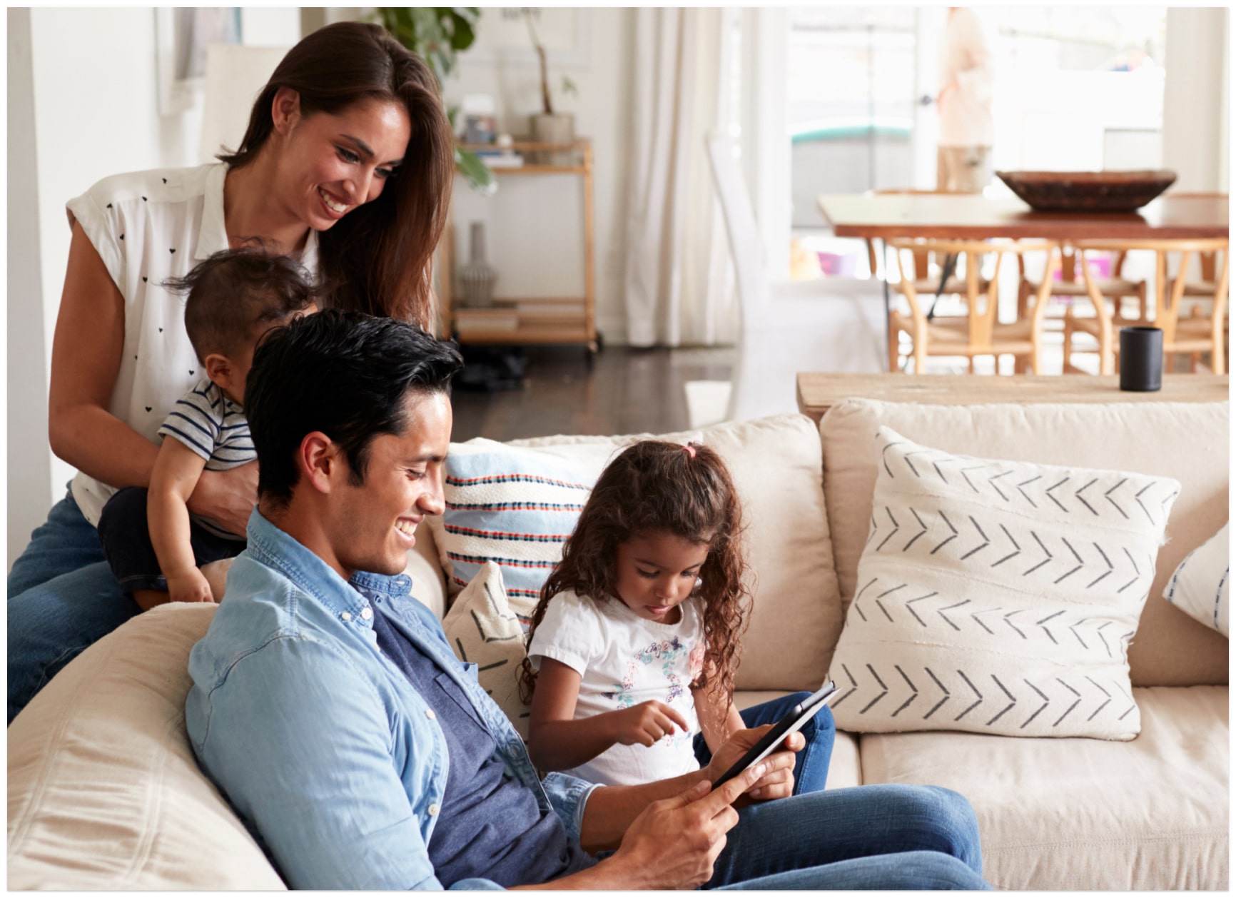 Smiling caregivers with two children sitting together and looking at a tablet screen.